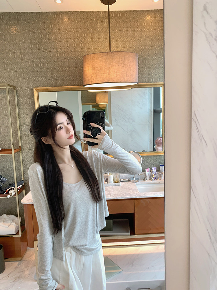 Woman taking mirror selfie wearing a gray long-sleeve top and white pants