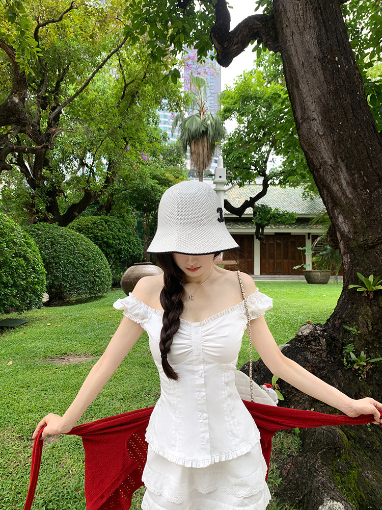 Woman wearing white off-shoulder dress and white bucket hat in a garden setting