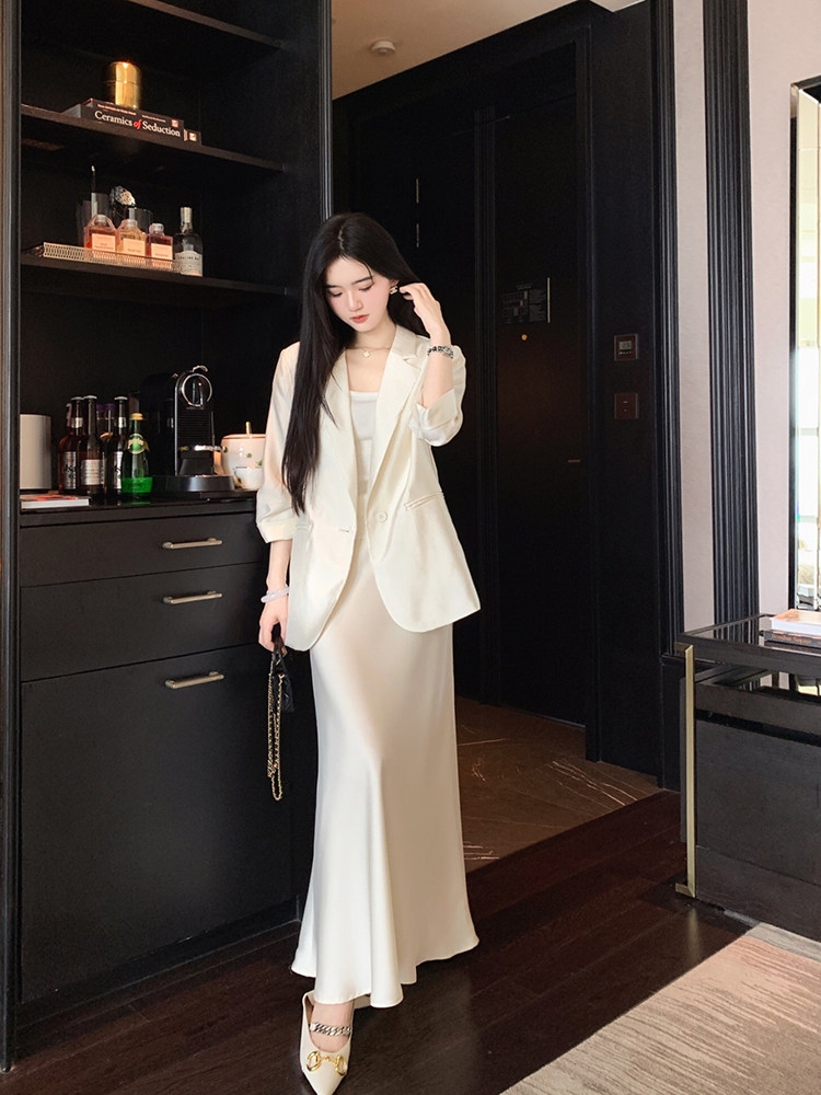 Woman wearing a cream-colored blazer and matching satin skirt in a modern interior setting