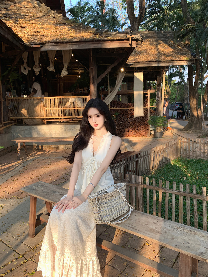 Woman wearing a white lace dress sitting on a wooden bench outdoors