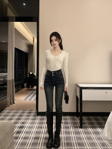 Woman wearing white ribbed long-sleeve top, dark high-waisted jeans, and black knee-high boots, holding a small black handbag.
