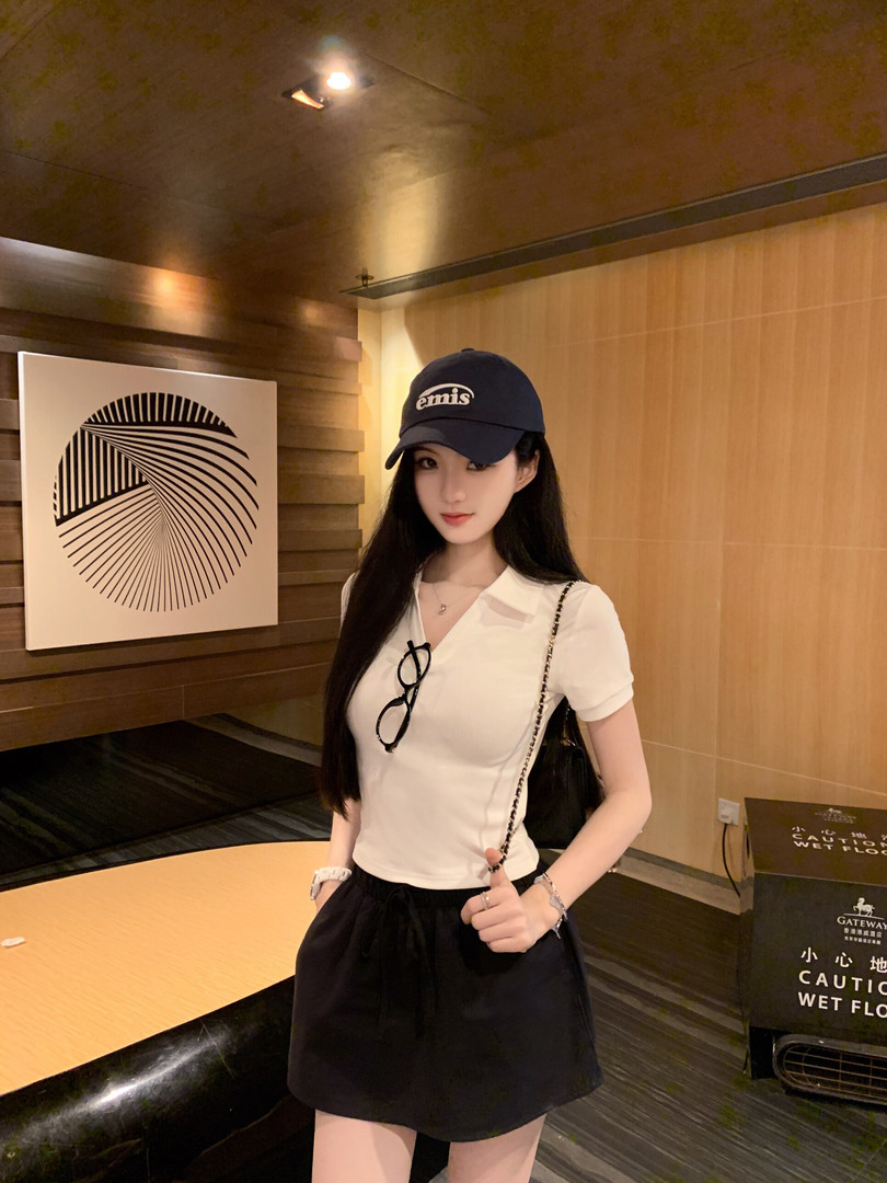 Woman wearing a white top, black skirt, and a navy cap with 'emis' logo, standing indoors.