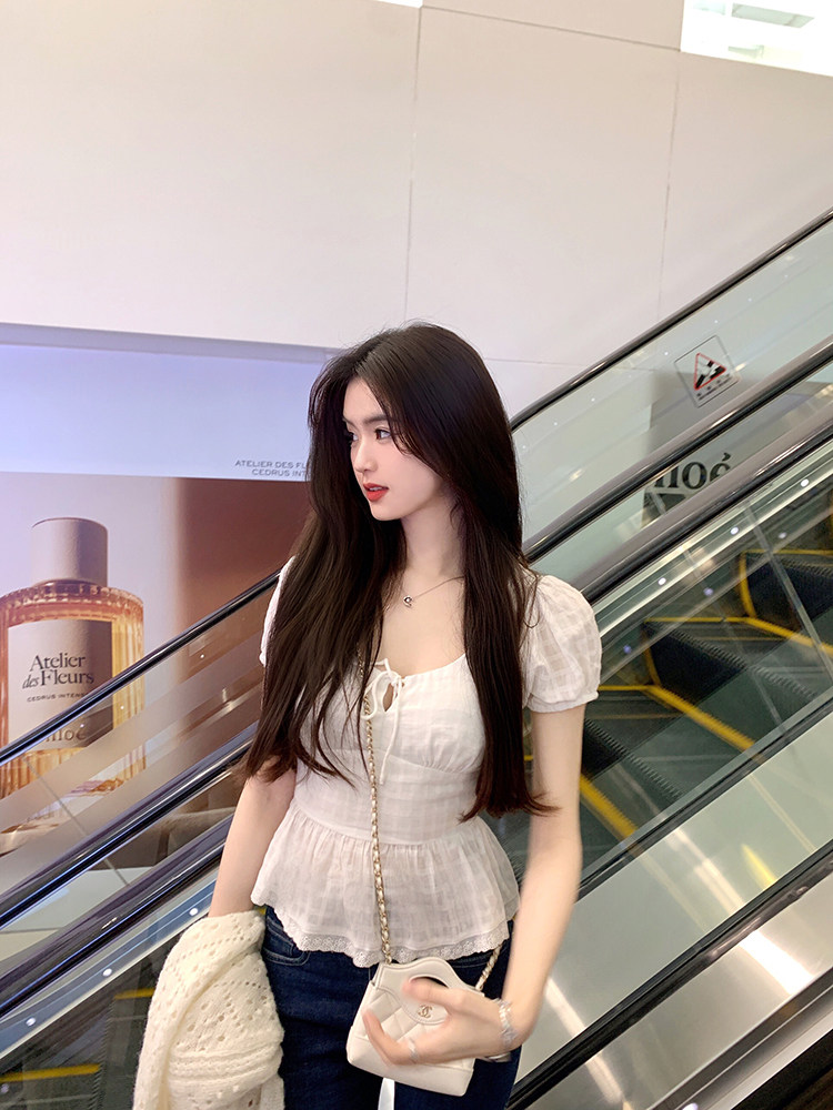 Woman wearing white peplum top with lace-up front, standing near escalator