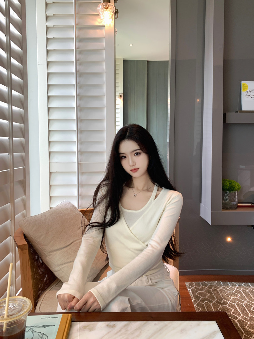 Woman wearing a cream-colored long-sleeve wrap top and matching pants, seated in a modern interior setting