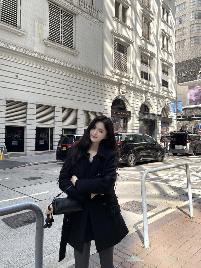 Woman wearing black coat and carrying black bag on city street