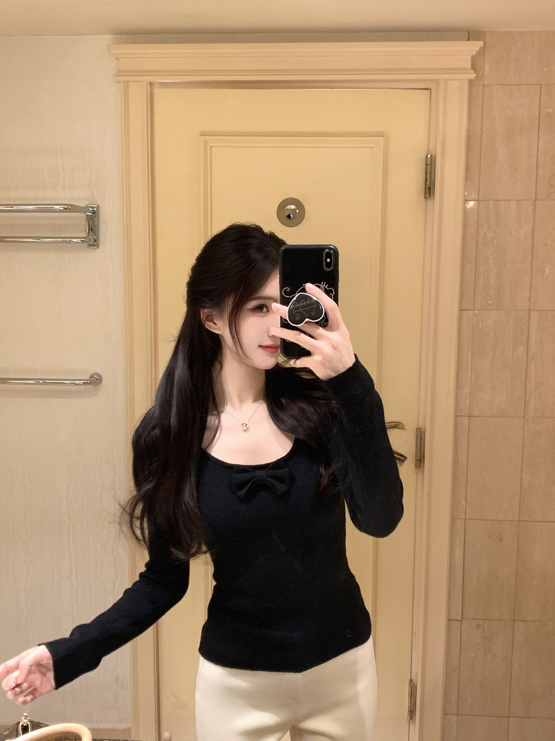 Woman taking mirror selfie wearing black top with bow detail and white pants
