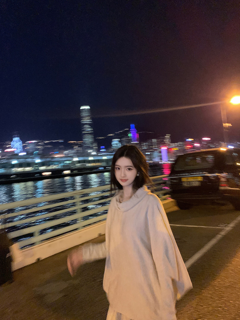 Woman wearing a light-colored oversized hoodie at night with city skyline in background