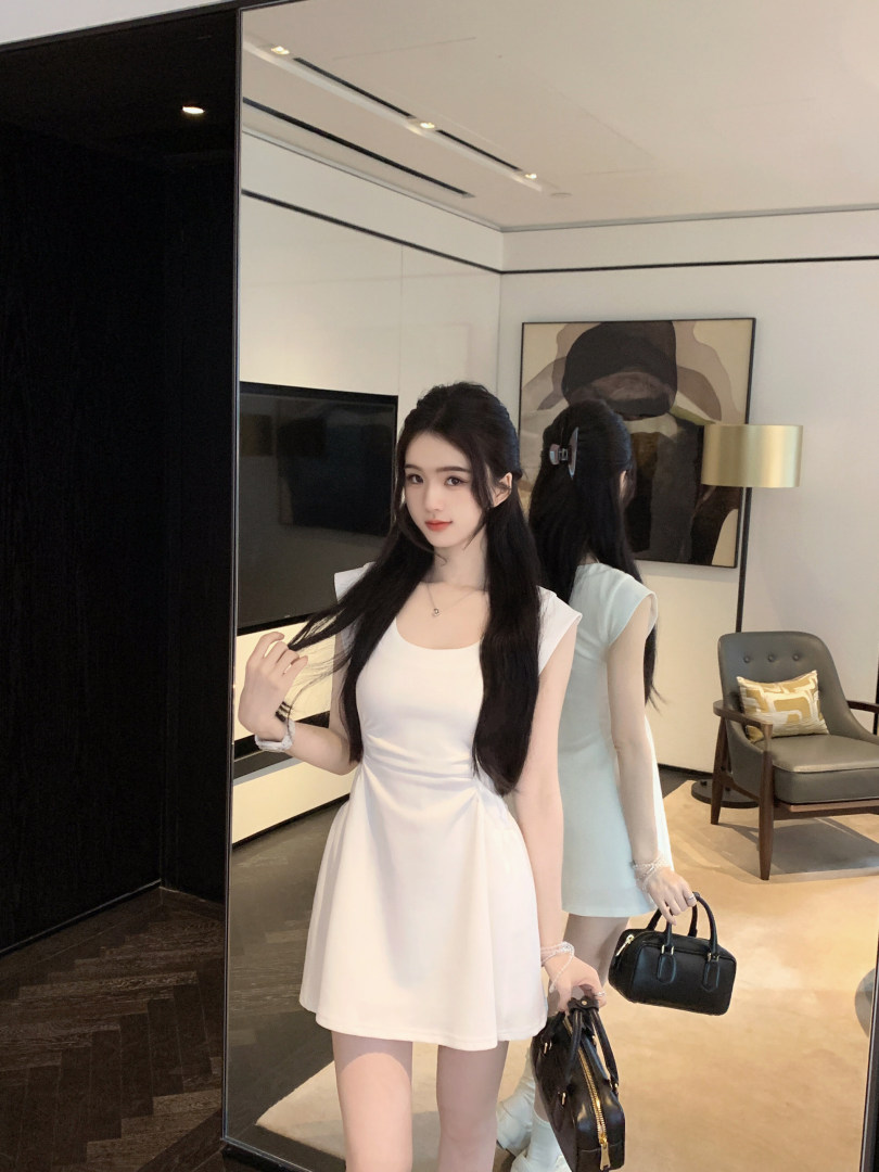 Woman wearing a white sleeveless dress standing in front of a mirror holding a black handbag