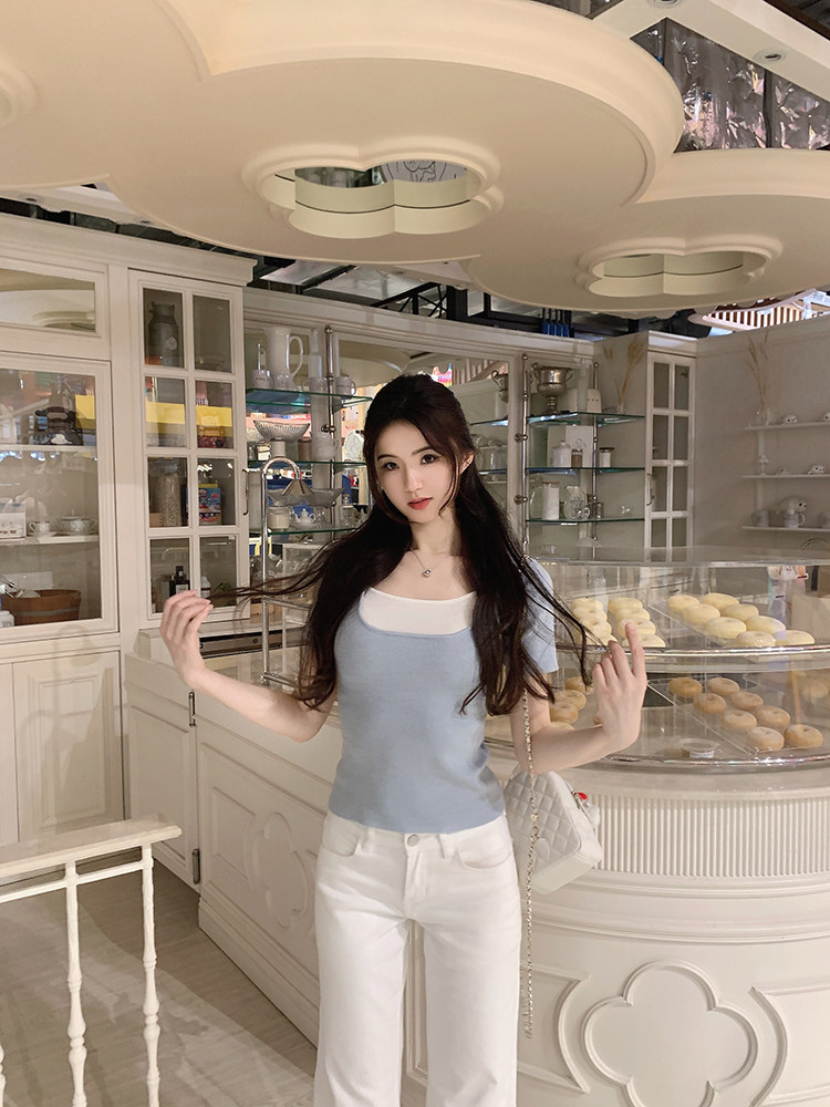 Woman wearing a light blue and white color-block top with white pants in a bakery setting
