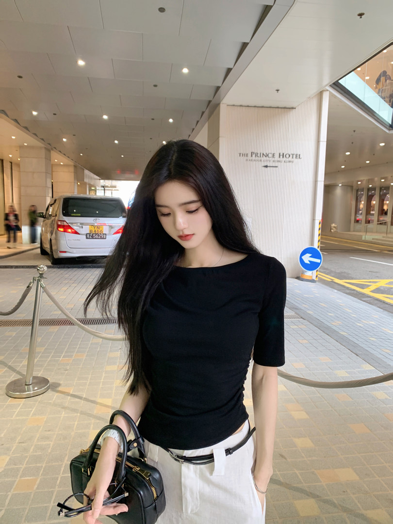Woman wearing a black short-sleeve top and white pants, holding a black handbag.