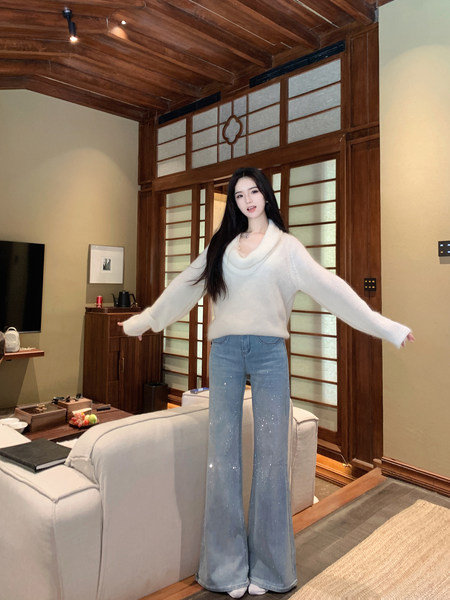 Woman wearing white knit sweater and sparkly wide-leg jeans in a wooden interior