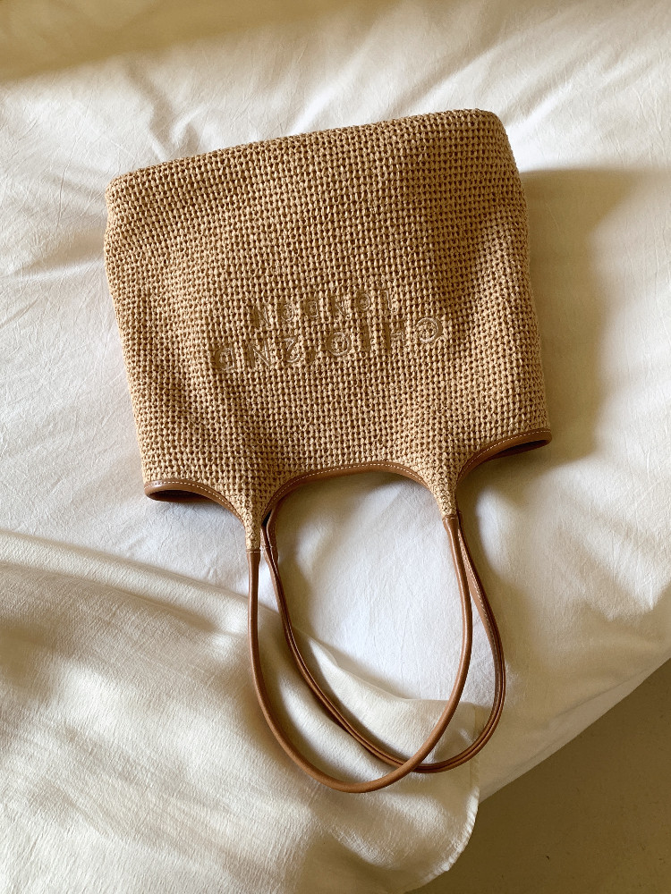 Woven straw tote bag with leather handles on white fabric background