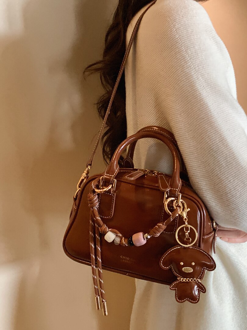 Brown leather handbag with charm and shoulder strap worn by a person