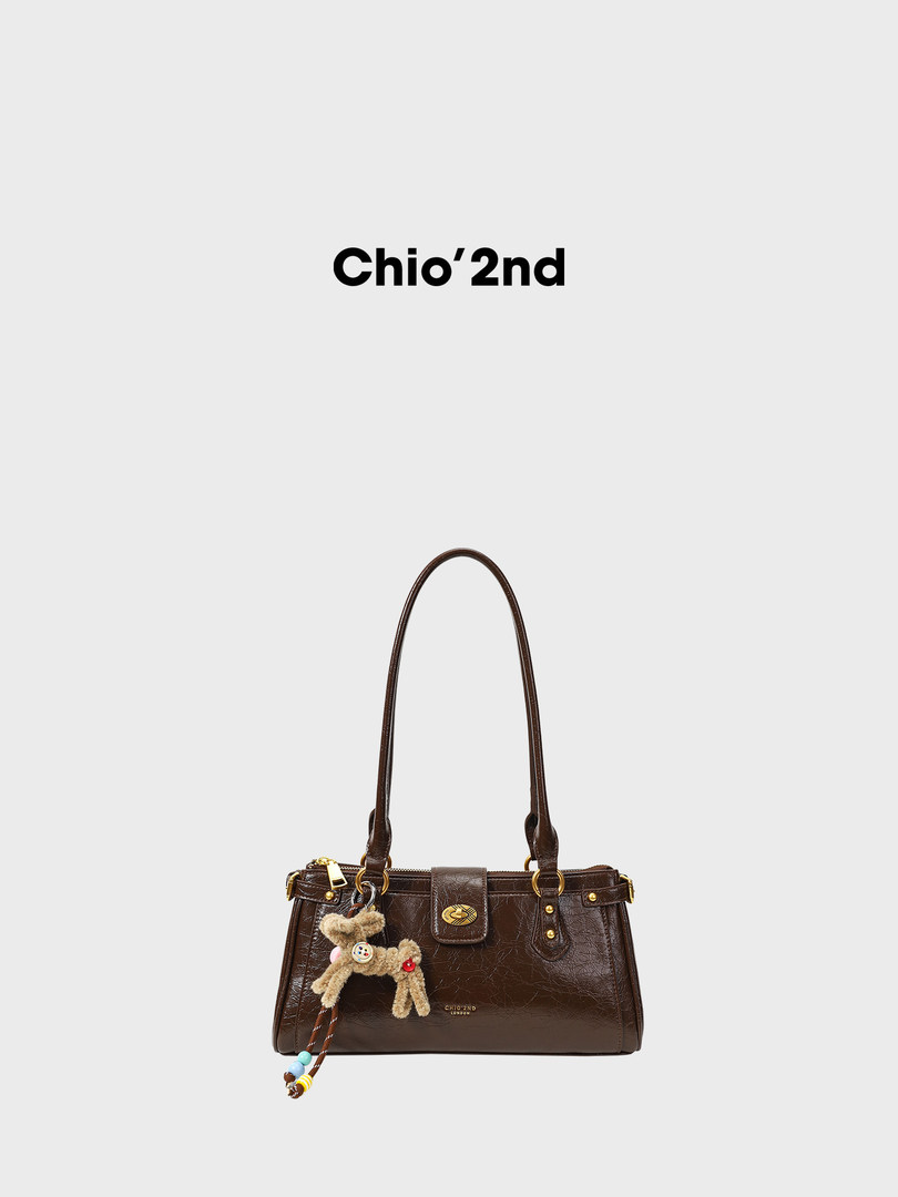 Brown leather shoulder handbag with a charm on a plain background