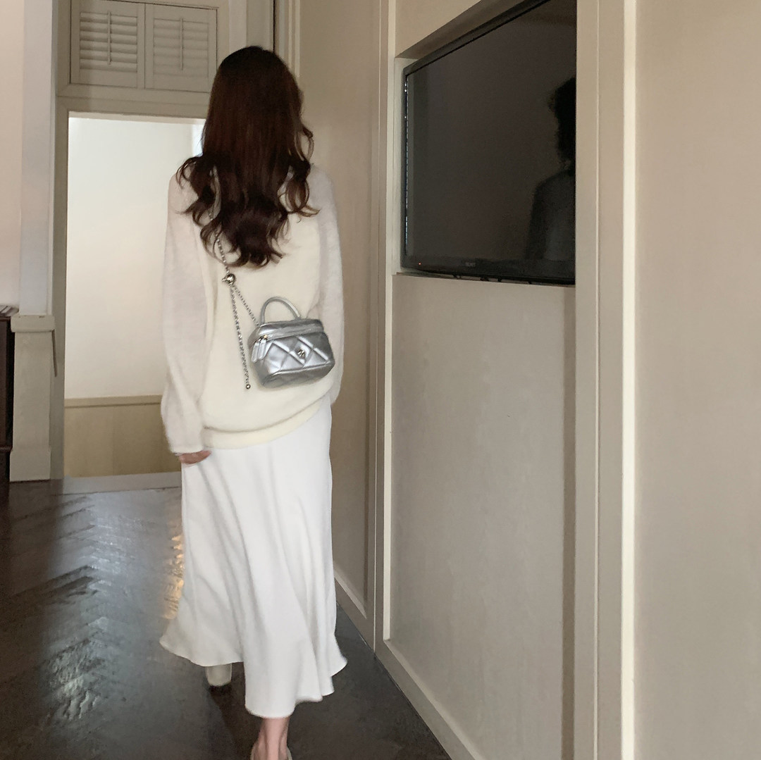 Woman wearing a cream outfit with a small silver chain-strap bag on her back