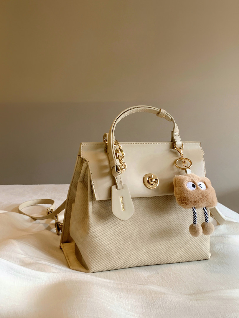Cream-colored structured handbag with gold hardware and a fluffy charm