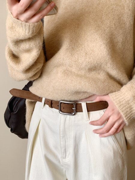 Model wearing a beige fuzzy sweater with white pants and a brown belt