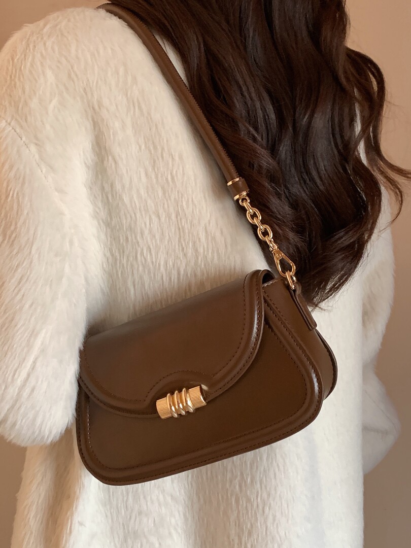 Brown leather shoulder bag worn crossbody on a model in a white fuzzy coat