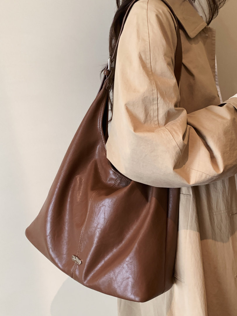 Brown leather shoulder bag worn with a beige trench coat