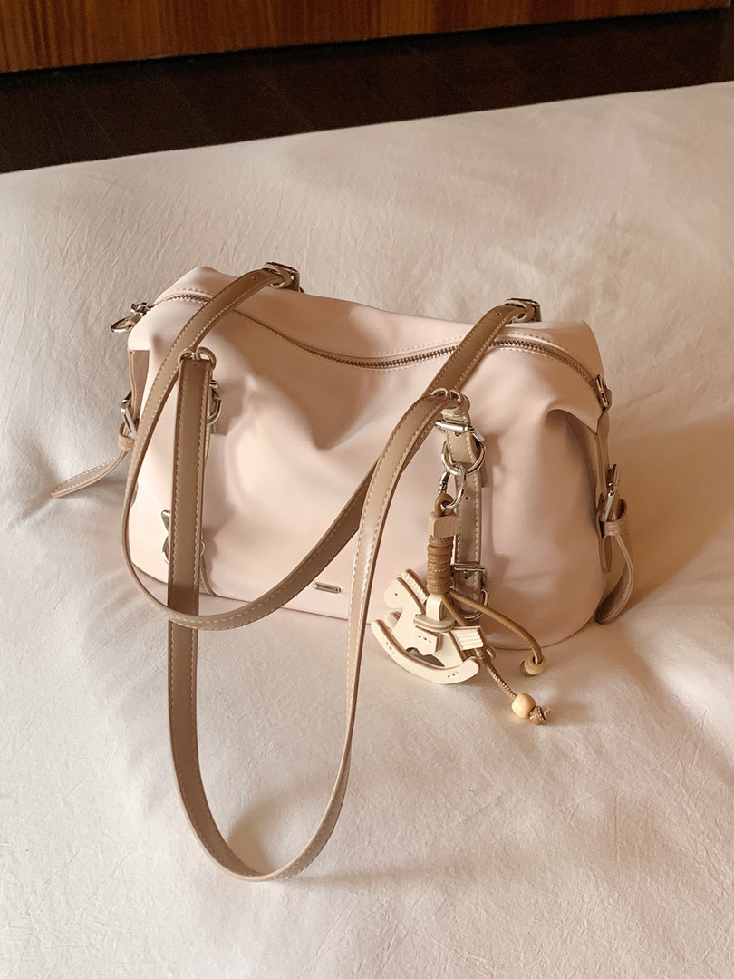 Light beige shoulder handbag with long straps and charm on a fabric surface