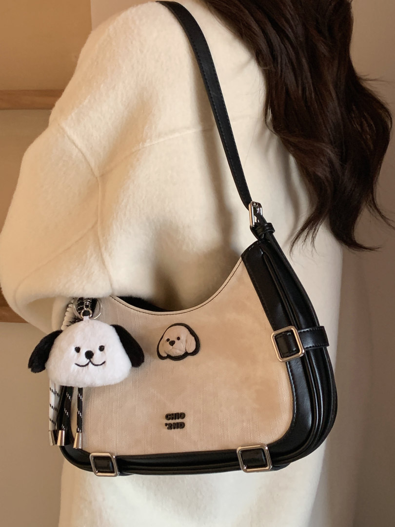 Cream and black shoulder bag worn by a model with a dog charm
