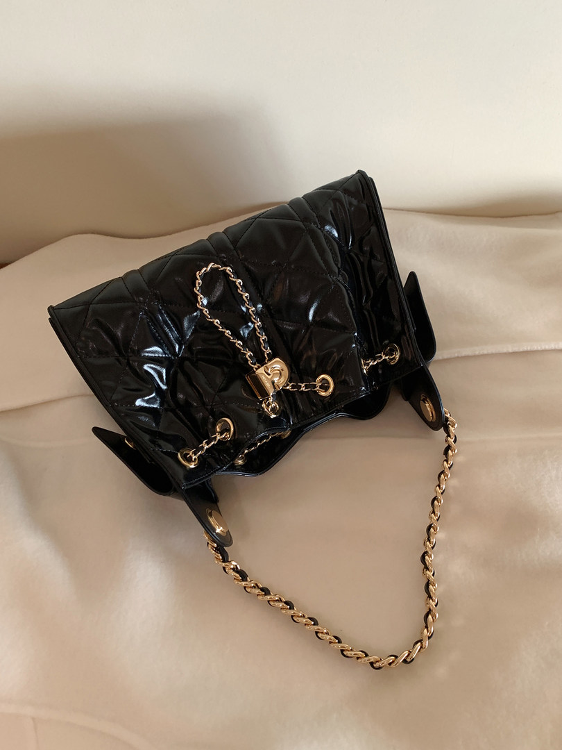 Black quilted chain-strap handbag on a light upholstered surface