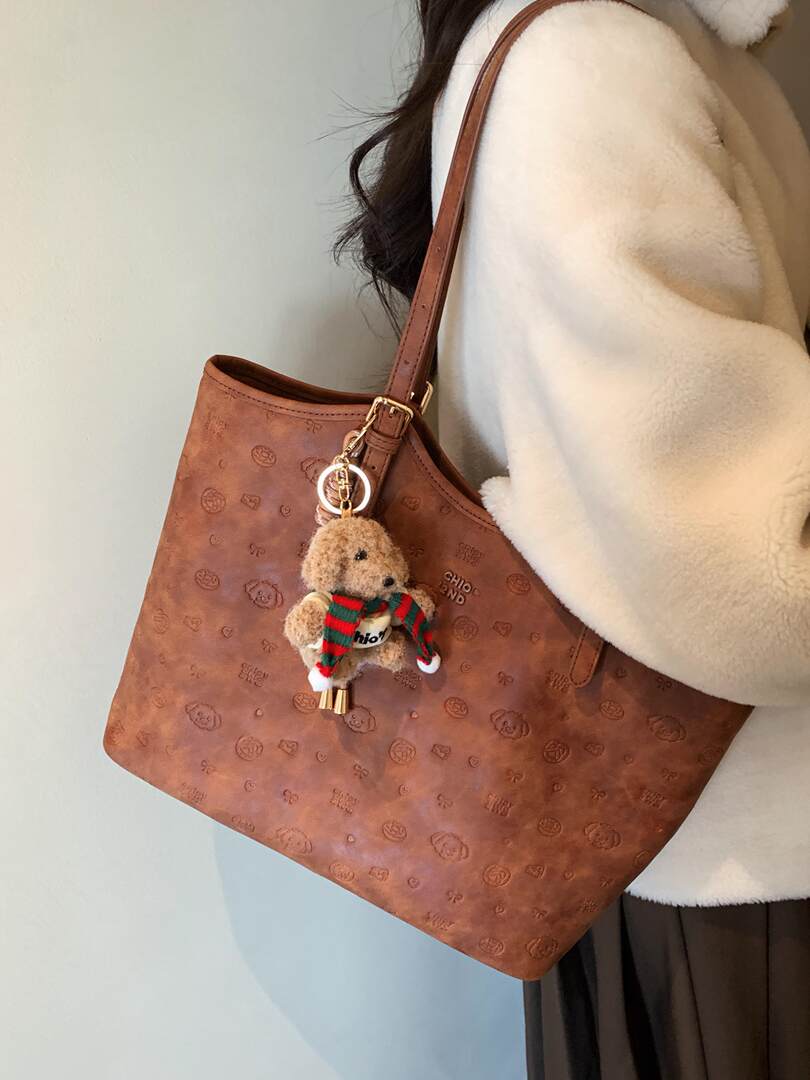 Brown leather shoulder tote bag with teddy bear charm worn on a model
