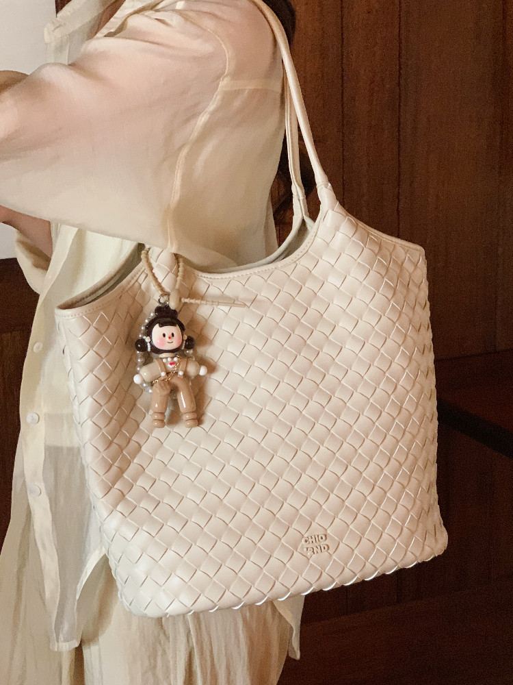 White woven tote bag with a charm, worn on a model