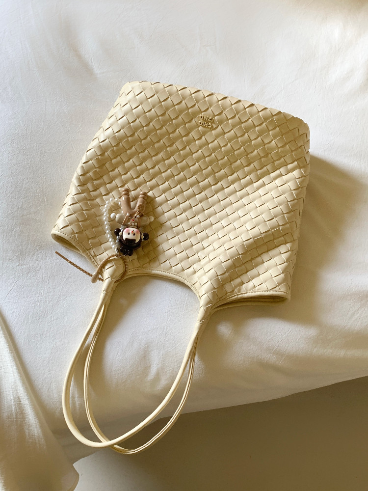 Beige woven tote bag on a white bed