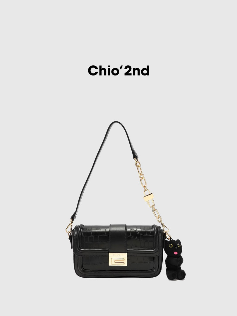 Black leather shoulder bag with gold chain strap and cat charm on a plain background