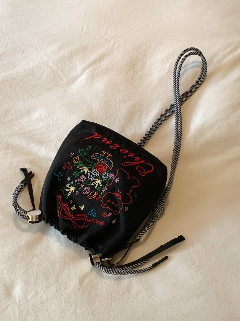 Black drawstring backpack with colorful embroidered design and braided straps