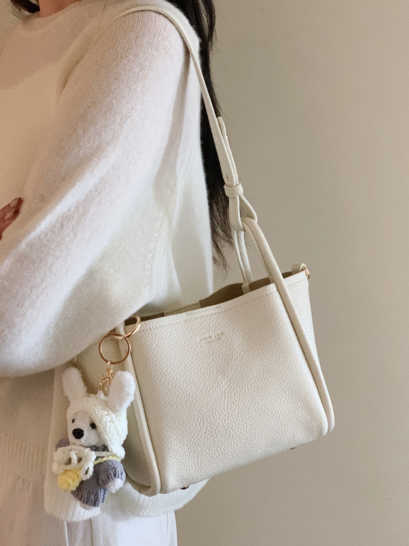 White textured shoulder handbag worn on a model with a plush keychain charm
