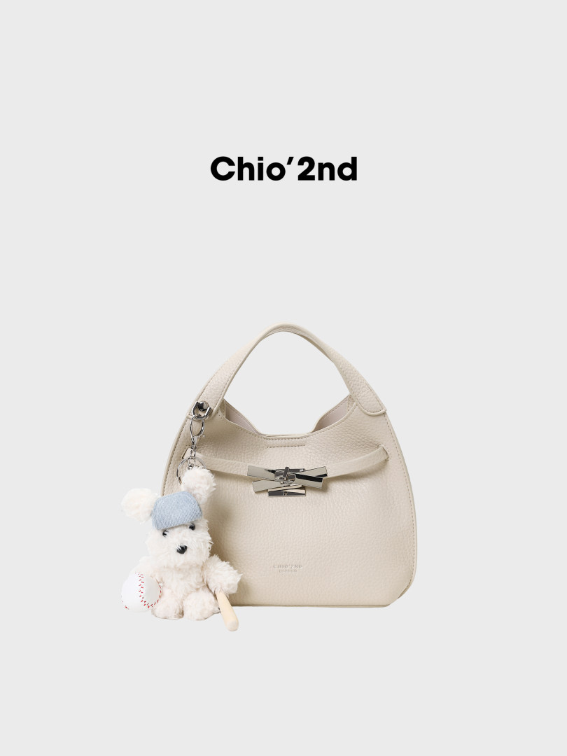 Cream textured handbag with a teddy bear charm on a white background