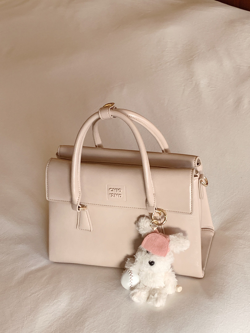 Light beige structured handbag with top handles and teddy bear charm