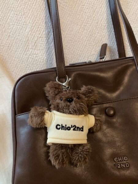 Brown leather handbag with teddy bear charm on a white background