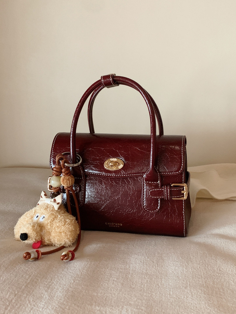 Burgundy structured leather handbag with gold hardware and a plush dog charm
