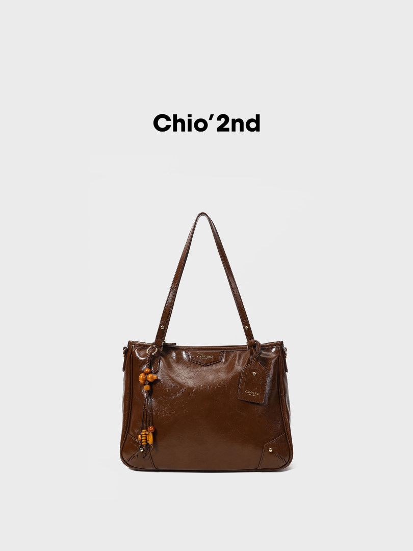 Brown leather tote handbag with long straps and charm detail on white background
