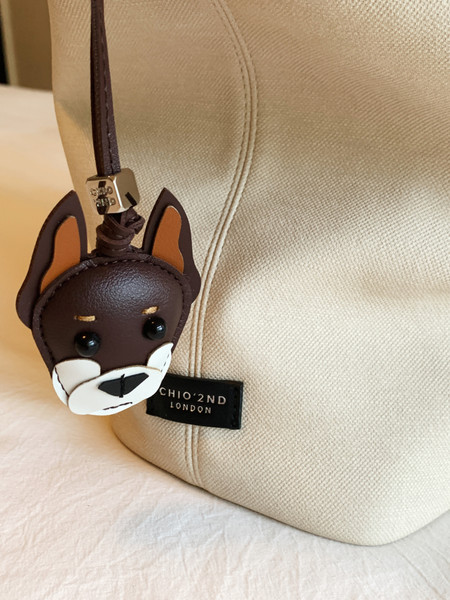 Beige textured handbag with a dog-face charm and logo tag