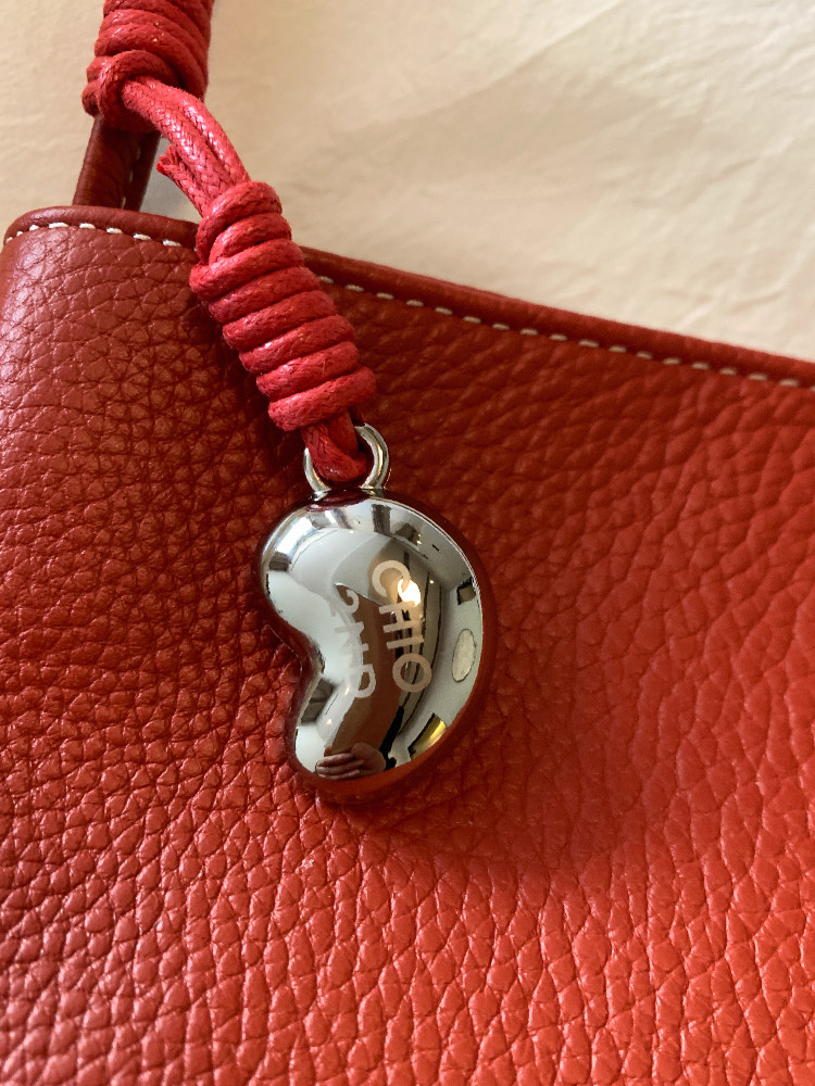 Close-up of a red leather handbag with a metal charm