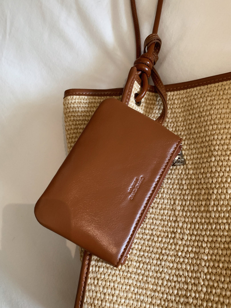 Brown leather pouch attached to a woven straw tote bag