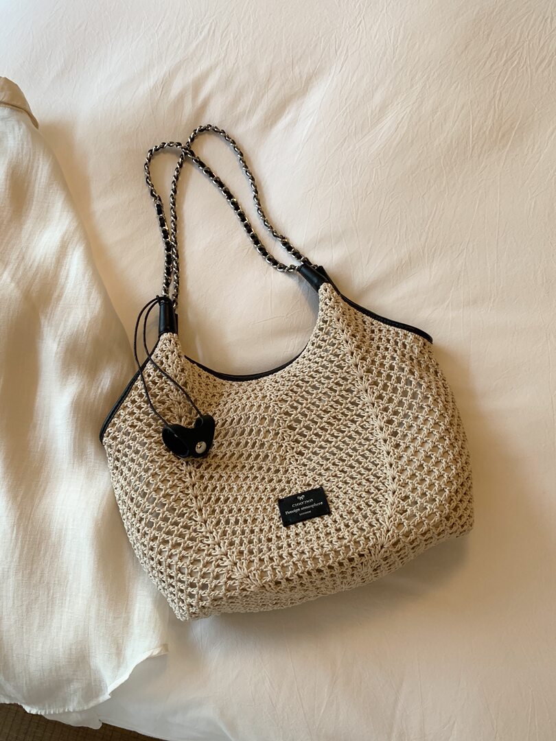 Beige woven tote bag with chain strap on a bed