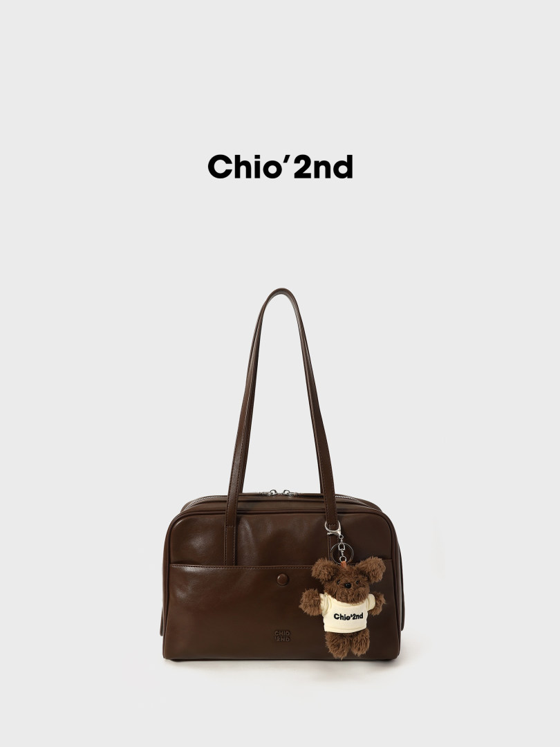 Brown leather handbag with long shoulder straps and a teddy bear charm on a white background