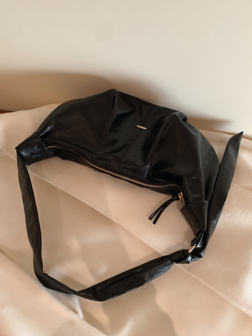Black leather shoulder bag laid on a bed