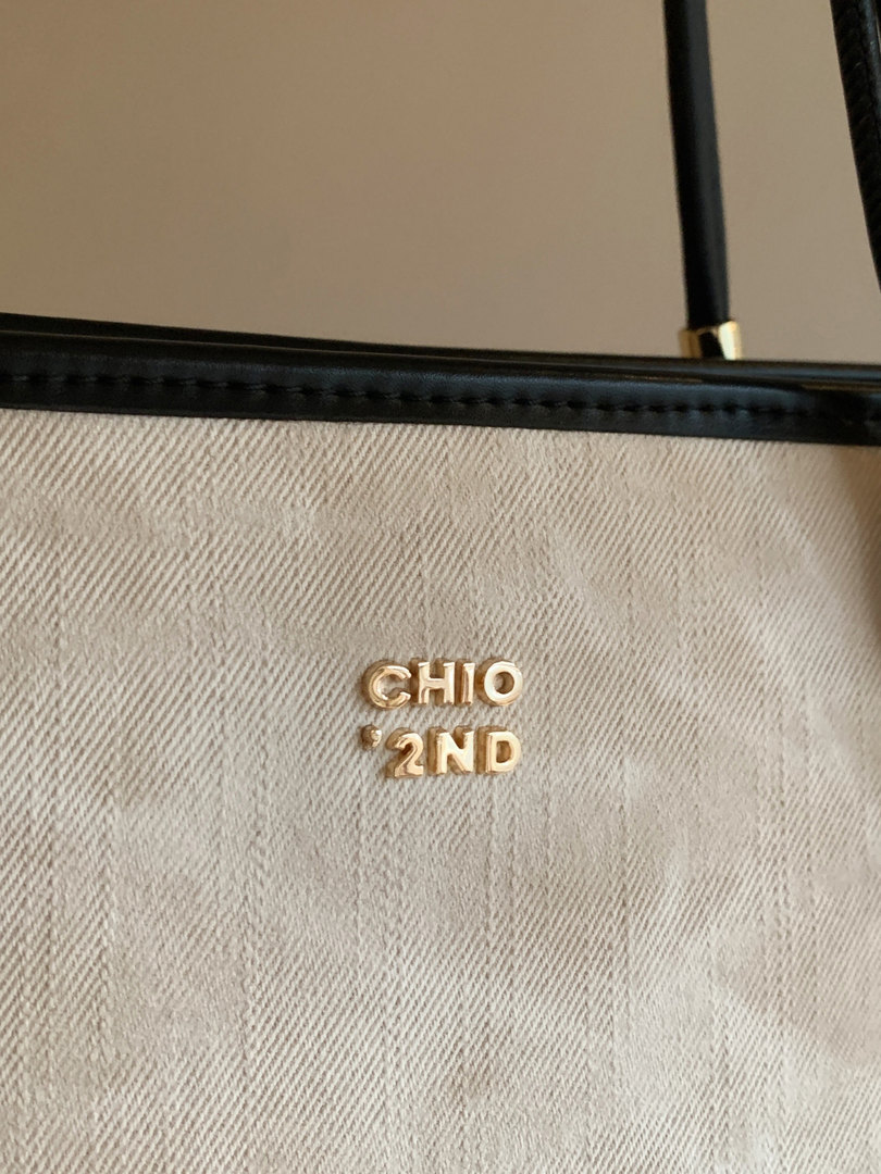 Close-up of a beige textured handbag with black trim and gold logo hardware