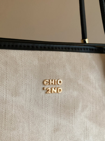 Close-up of a beige textured handbag with black trim and gold logo hardware