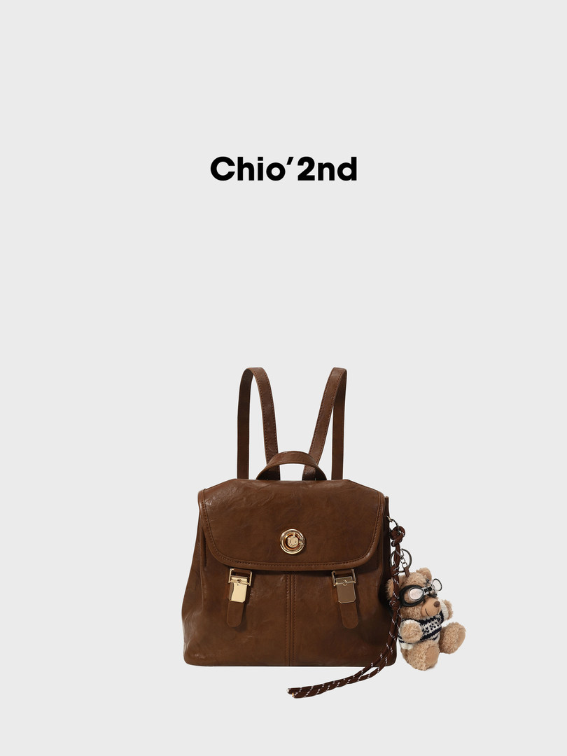 Brown leather backpack with a teddy bear charm on a white background