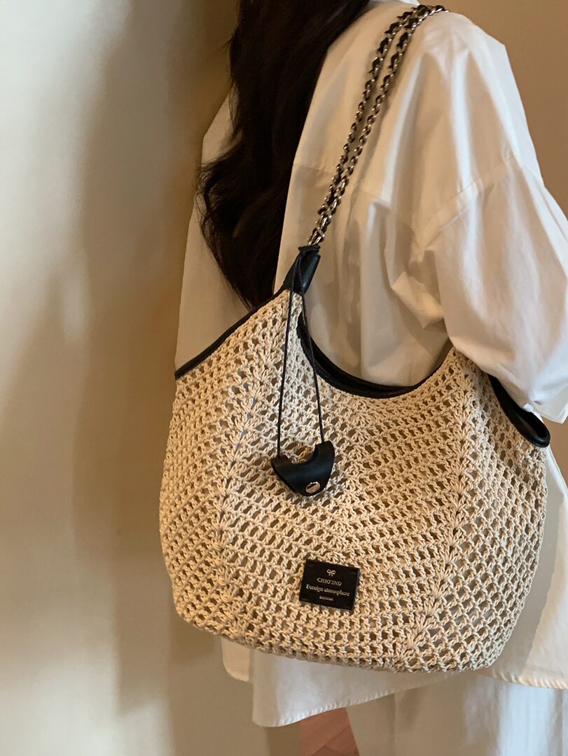 Woven straw tote bag with chain strap worn on a person