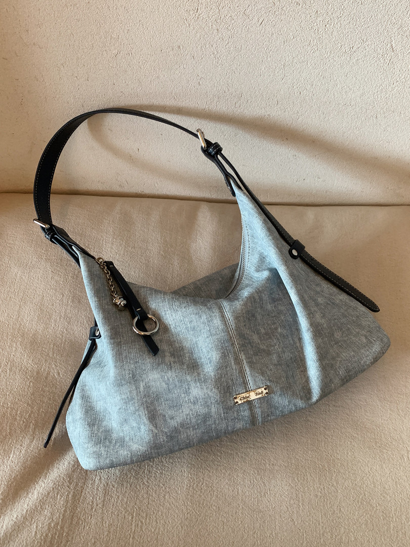Light blue denim shoulder handbag with black straps on a beige surface