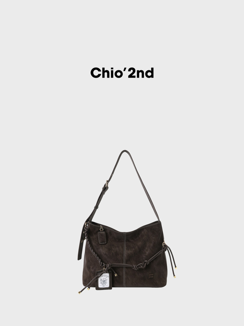 Black shoulder handbag with long strap and decorative tags on a plain background