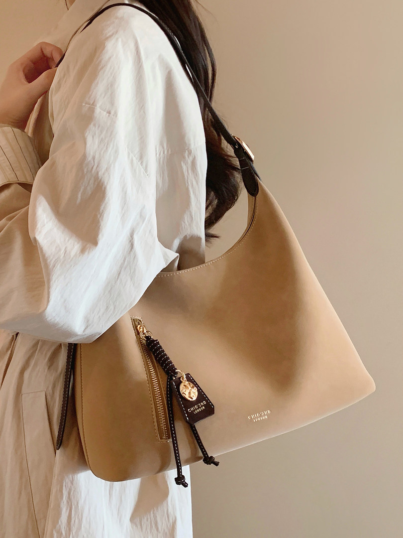 Beige leather tote handbag with gold zipper and black drawstring tassels being held by a model